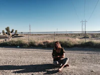 a woman sitting on the ground in front of a joshua tree