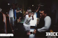 a group of people in a room with a man in a hat